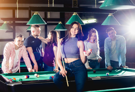 Young woman playing in billiard. Posing near the table with a cue in her hands