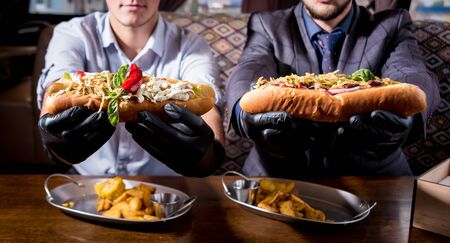 Two hungry young men eating a hot dogs in cafe. Background. Restaurantの写真素材