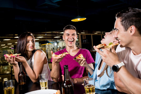 Cheerful friends in the pub. Drinking beer, eating pizza, talking, having fun.