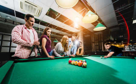 Group of young cheerful friends playing billiards.
