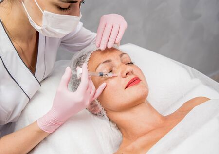 The doctor cosmetologist makes the facial injections procedure. Young woman in a beauty salon. Cosmetology concept.の写真素材