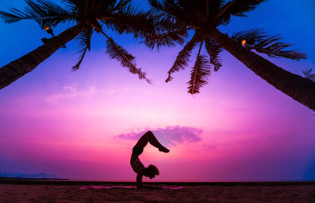 Beautiful young woman practic yoga at the beach. Early morning exercise. Sunrise. Palms background