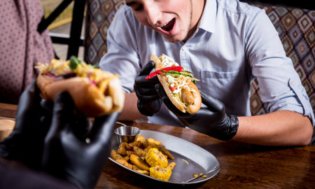 Two hungry young men eating a hot dogs in cafe. Background. Restaurant