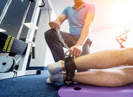 Rehabilitation therapy. Young man doing exercises on mat under supervision of physiotherapist....