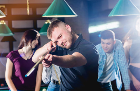 Young man playing in billiard. Posing near the table with a cue in his hands