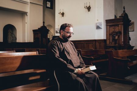 A monk in robes with holy bible in their hands praying in the churchの写真素材