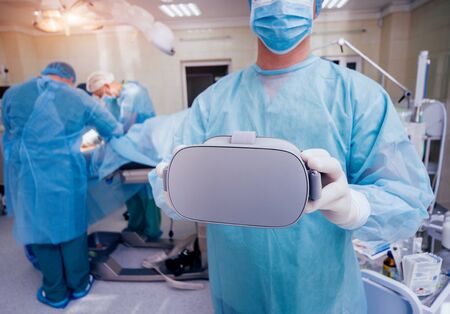 Doctor in a surgical room with virtual reality glasses on the background of the real operation. Modern technologiesの写真素材