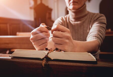 Christian woman praying in church. Hands crossed and Holy Bible on wooden desk.の写真素材