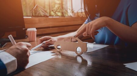 Man signing a car insurance policy, the agent is holding the wooden car model.の写真素材