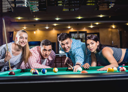 Group of young cheerful friends playing billiards.