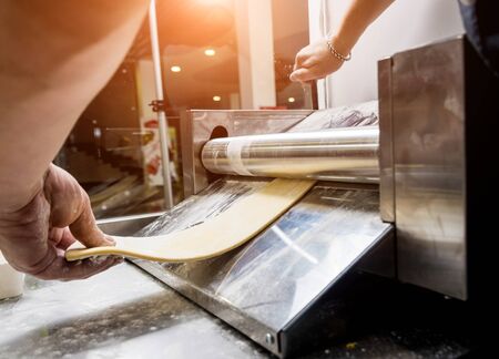 Chef rolling dough with a pasta machine. Pasta maker machine. Homemade italian style cuisine. Restaurant. Backgroundの写真素材