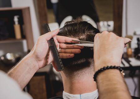 Young man with trendy haircut at barber shop. Barber does the hairstyle and beard trim. Concept barbershop.の写真素材