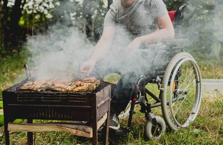 Disabled man resting in a campsite with friends. Wheelchair in the forestの写真素材