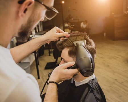 Young man with trendy haircut at barber shop. Barber does the hairstyle and beard trim. Concept barbershop.の写真素材