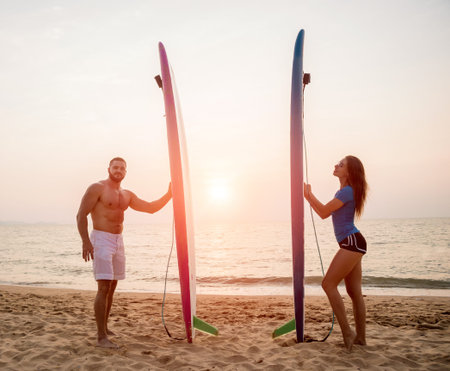 Silhouette of surfers couple holding long surf boards at sunset on tropical beachの写真素材