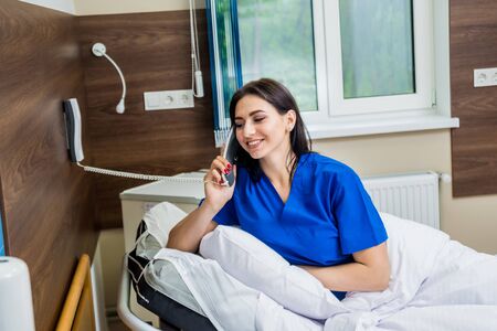 Patient talking on the phone in hospital bed. Young caucasian woman.の写真素材