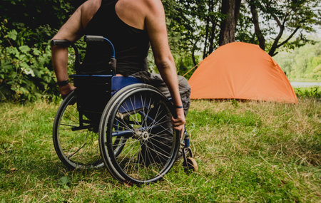 Disabled man resting in a campsite with friends. Wheelchair in the forest on the background of...