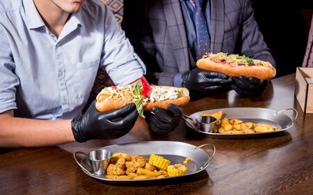 Two hungry young men eating a hot dogs in cafe. Background. Restaurantの写真素材