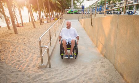 Disabled man in a wheelchair moves on a ramp to the beach.の写真素材