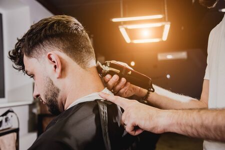Young man with trendy haircut at barber shop. Barber does the hairstyle and beard trim. Concept barbershop.の写真素材