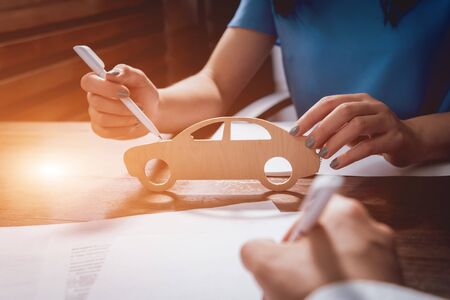 Man signing a car insurance policy, the agent is holding the wooden car model.の写真素材