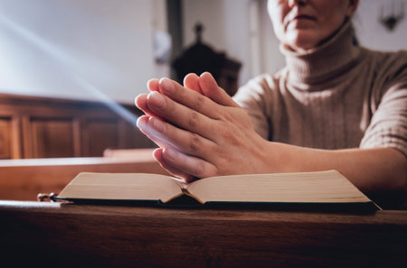 Christian woman praying in church. Hands crossed and Holy Bible on wooden desk.