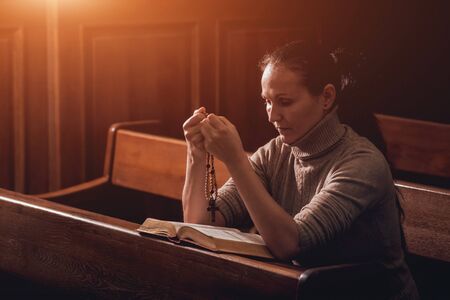 Christian woman praying in church. Hands crossed and Holy Bible on wooden desk.の写真素材