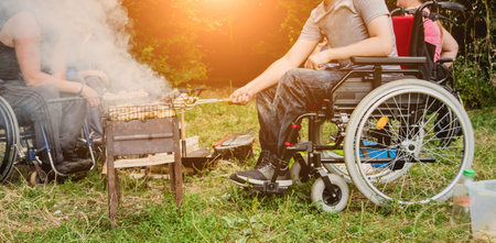 Disabled man resting in a campsite with friends. Wheelchair in the forest on the background of...