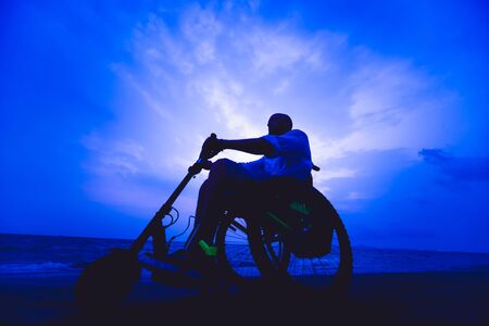 Disabled man in a wheelchair on the beach. Silhouette at sunset.の写真素材