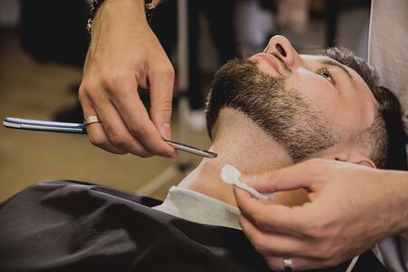 Young man with trendy haircut at barber shop. Barber does the hairstyle and beard trim. Concept barbershop.の写真素材