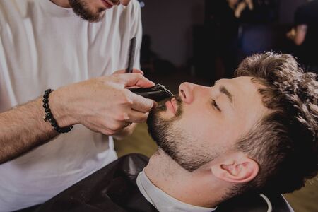 Young man with trendy haircut at barber shop. Barber does the hairstyle and beard trim. Concept barbershop.の写真素材