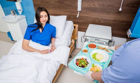 Nurse in medical coat is holding a tray with breakfastの写真素材