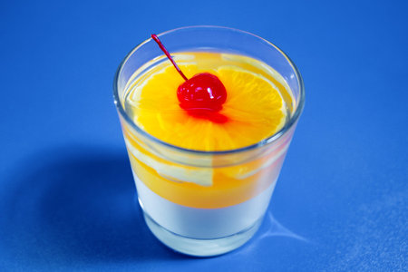 Jelly with cherry in glass on the blue table. Isolated
