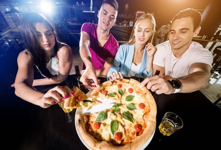 Cheerful friends in the pub. Drinking beer, eating pizza, talking, having fun.の写真素材