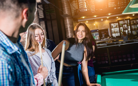 Group of young cheerful friends playing billiards.