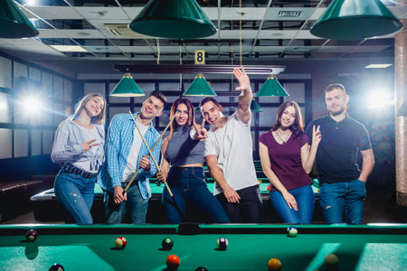 Group of young cheerful friends playing billiards.