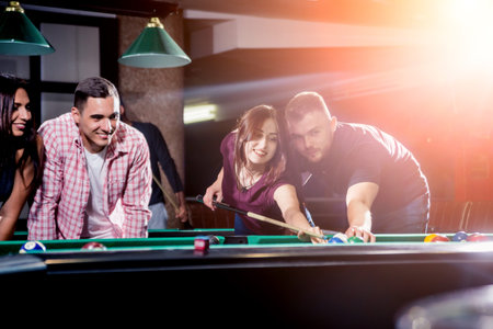 Group of young cheerful friends playing billiards.