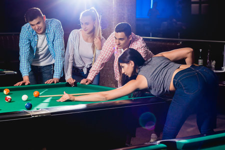 Group of young cheerful friends playing billiards.