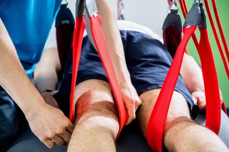 Physiotherapy. Suspension training therapy. Young man doing fitness traction therapy with suspension-based exercise training system. Treatment of pain in the spine.の写真素材