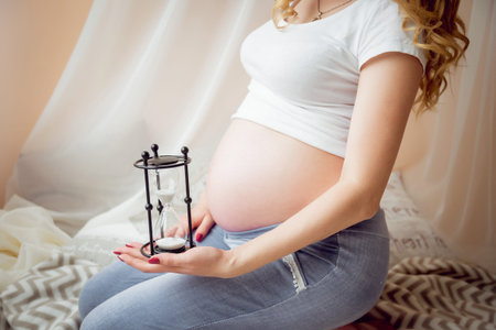 Young pregnant woman near a window. Light background