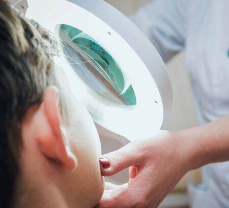 Concentrated dermatologist using medical loupe in the clinic. Medical equipmentの写真素材