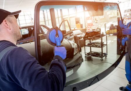Automobile special workers replacing windscreen or windshield of a car in auto service station garage. Backgroundの写真素材