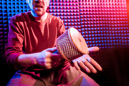 Young man playing on maracas in sound recording studio. Modern background
