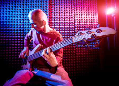 Young man playing on the bass guitar in sound recording studio. Modern background