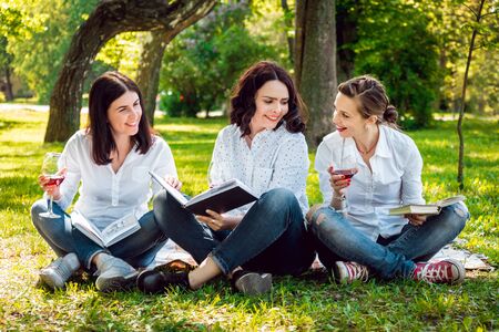 Young beautiful girls with glass of red wine and books in the park.の写真素材