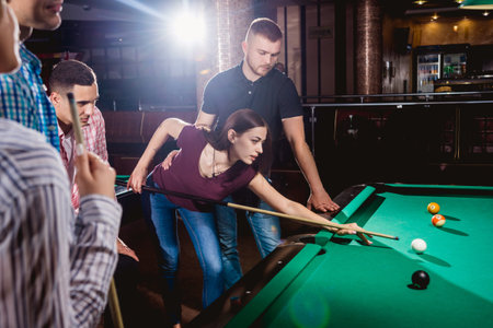 Group of young cheerful friends playing billiards.