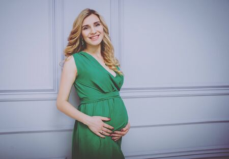 Young pregnant woman near the wall. Light background.の写真素材