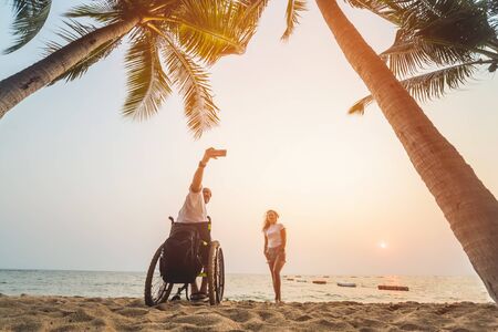 Disabled man in a wheelchair with his wife on the beach.の写真素材