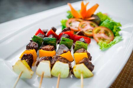 Meat on skewer with grilled vegetables on white plate. Restaurantの写真素材