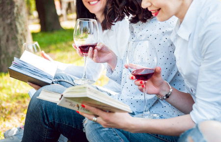 Young beautiful girls with glass of red wine and books in the park. Nature backgroundの写真素材